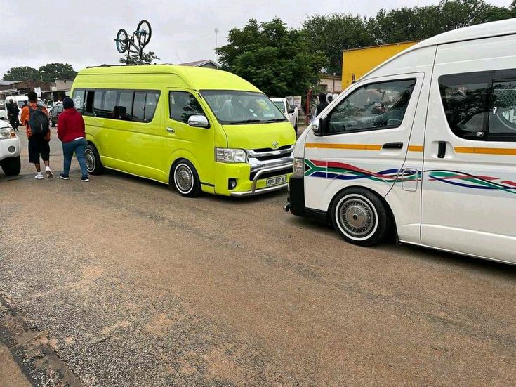 two vans parked next to each other on a road with people standing in the background