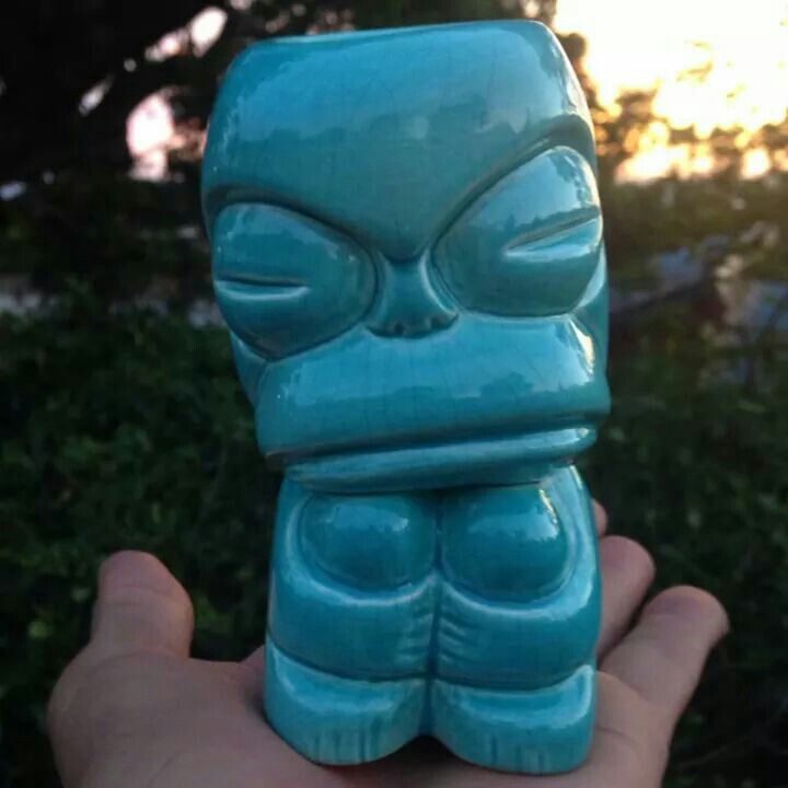 a hand holding a blue ceramic statue in the shape of a tiki head with eyes