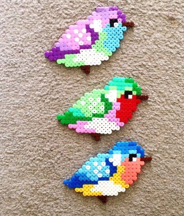 three colorful birds sitting on top of a floor next to each other and one is made out of perler beads