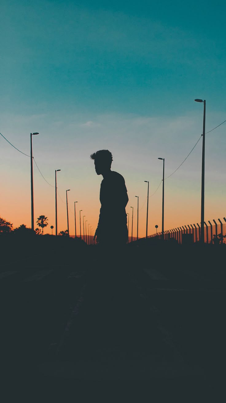 the silhouette of a person standing in front of a fence and street lights at sunset