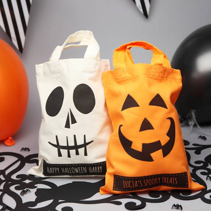 two halloween bags sitting next to each other on a table with balloons in the background