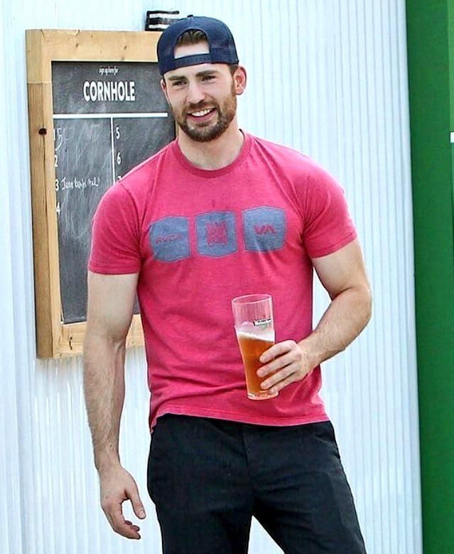 a man holding a glass of beer in front of a chalkboard