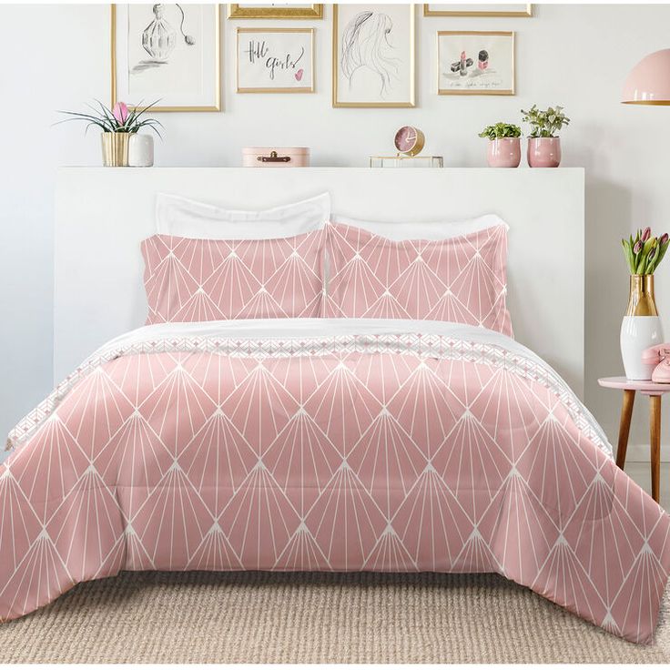 a bed with pink comforter and pillows in a room next to pictures on the wall