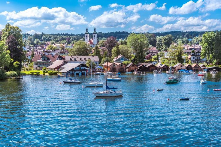 boats are floating on the water in front of small houses and trees with blue sky