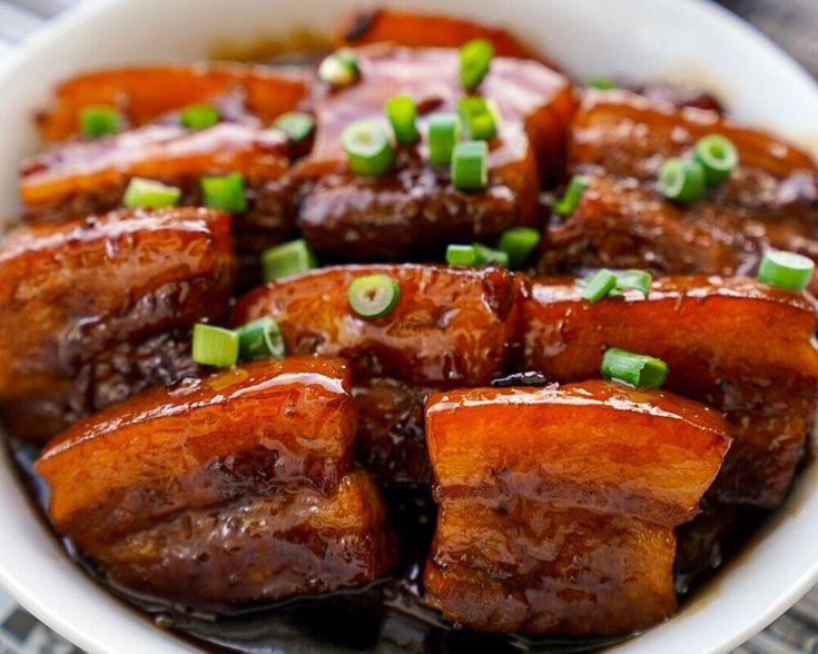 a white bowl filled with meat covered in sauce and green onions