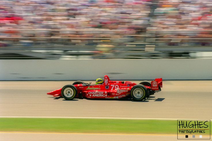 a man driving a red race car down a track in front of a large crowd