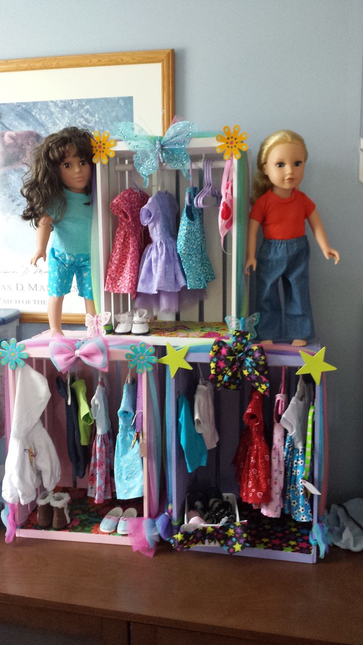 two dolls are standing on top of a shelf filled with clothes and other doll accessories