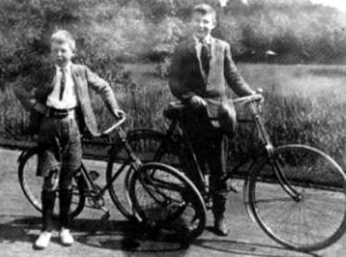 an old black and white photo of two young boys on bicycles in front of a pond