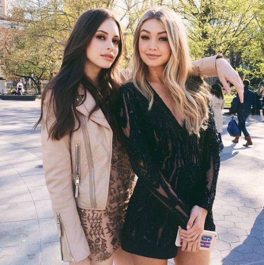 two beautiful young women standing next to each other on a city street with trees in the background