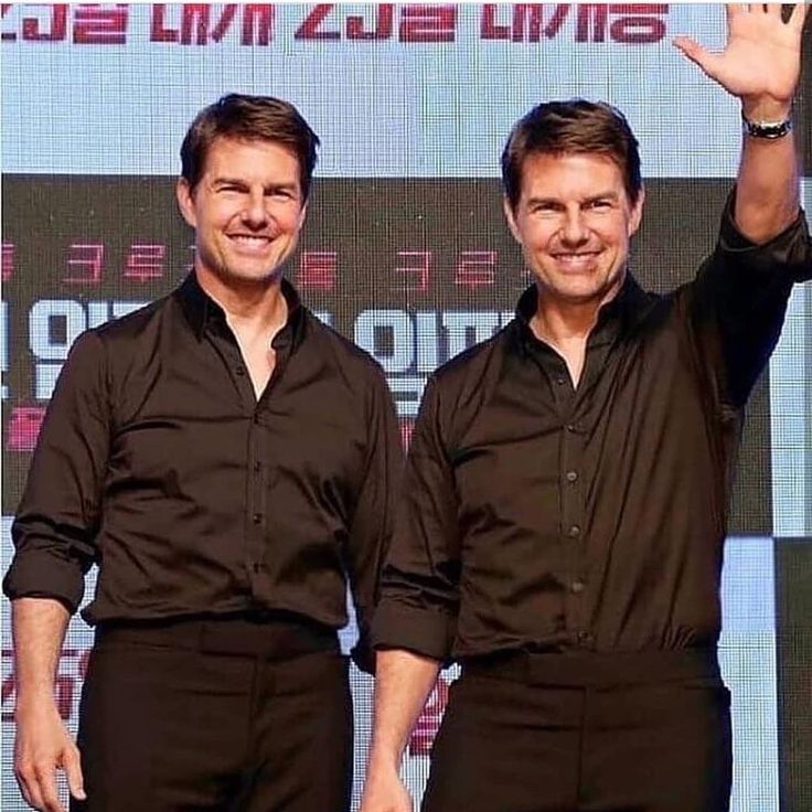 two men standing next to each other in front of a screen with their hands up