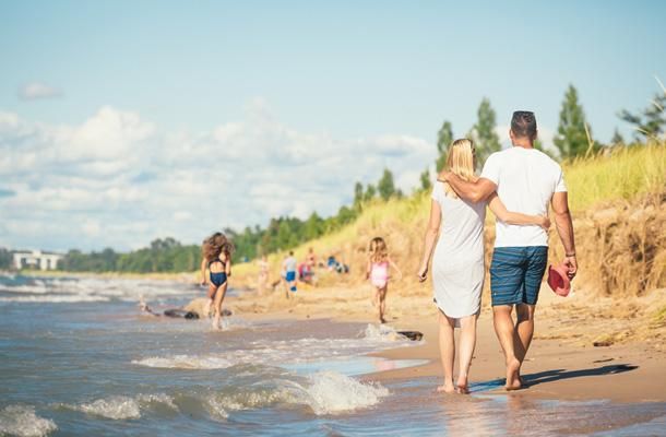 a man and woman walking along the beach towards the ocean while others play in the water