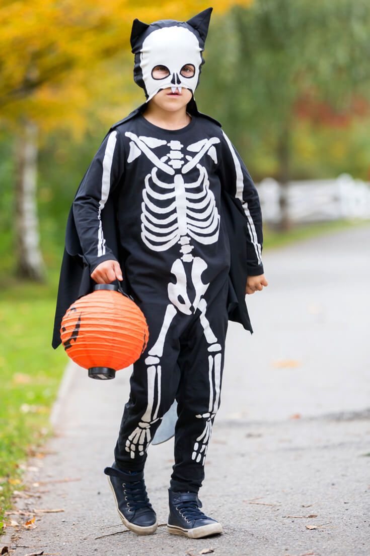 a little boy dressed up as a skeleton with a cat mask and holding a pumpkin