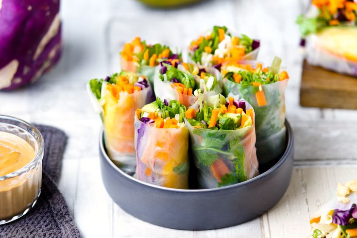 there are many colorful rolls in the bowl on the table next to some dipping sauce