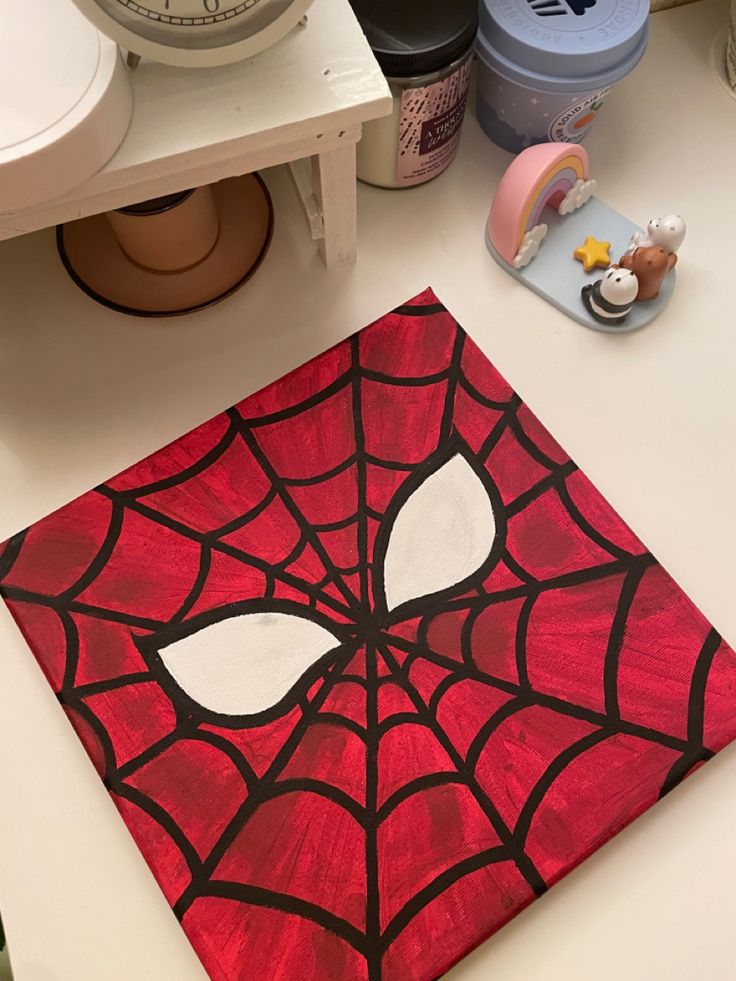 a spiderman face painted on a red piece of paper next to a clock and other items