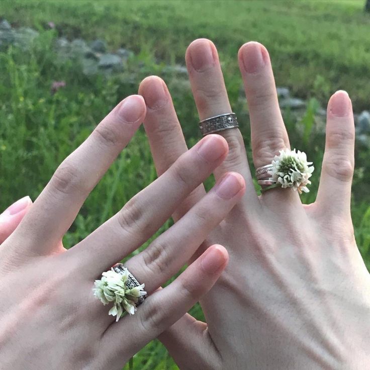 two hands with wedding rings and flowers on their fingers in front of a grassy field