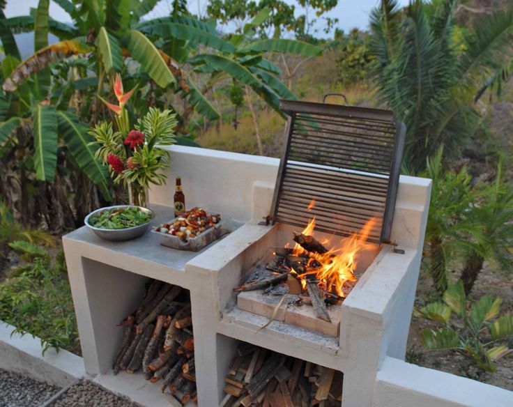 an outdoor bbq grill with fire and food on the outside, surrounded by tropical vegetation