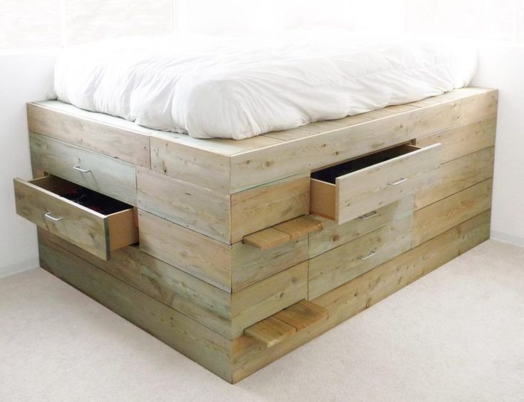 a bed made out of pallet wood with two drawers on each side and a white comforter