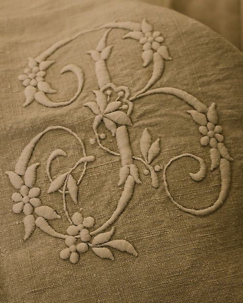 an embroidered monogram is shown on the back of a linen pillow cover with flowers and vines