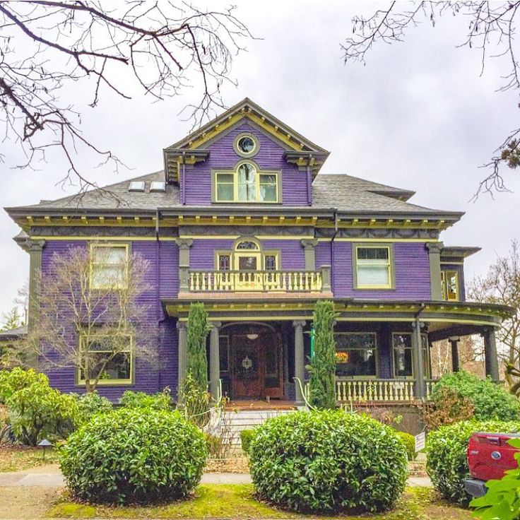 a large purple house with lots of trees and bushes around it's front entrance