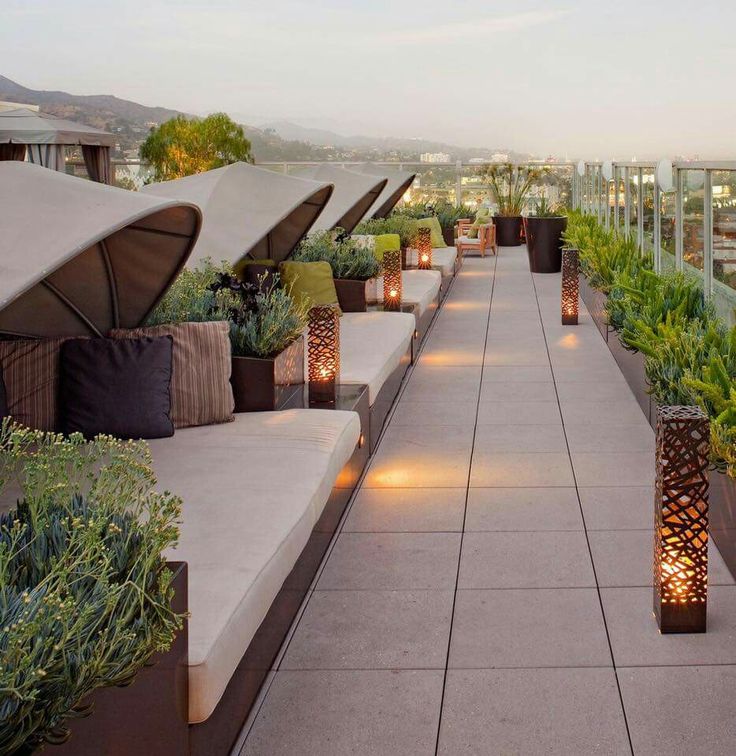 an outdoor seating area with candles lit up on the benches and potted plants along the walkway