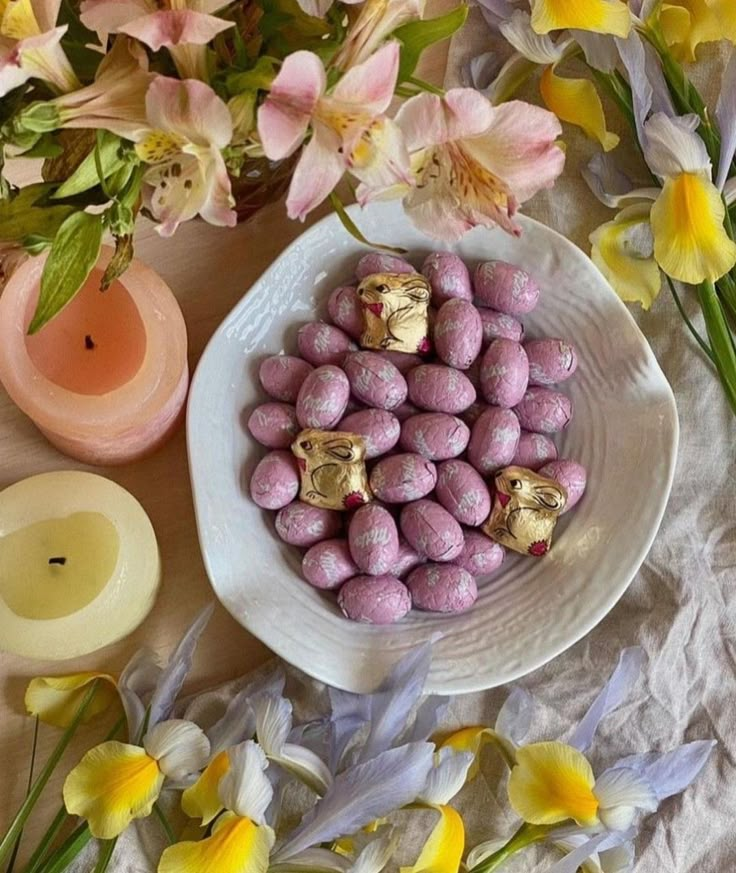 a bowl filled with chocolate eggs next to flowers and candles on a white table cloth