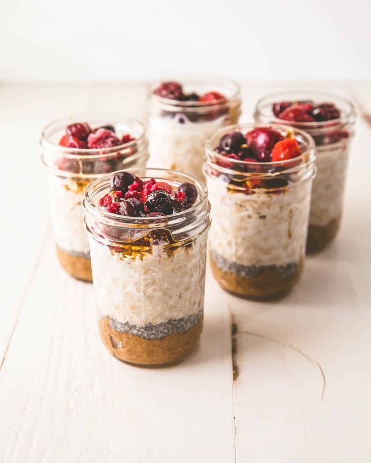 four jars filled with oatmeal and berries on top of a white table