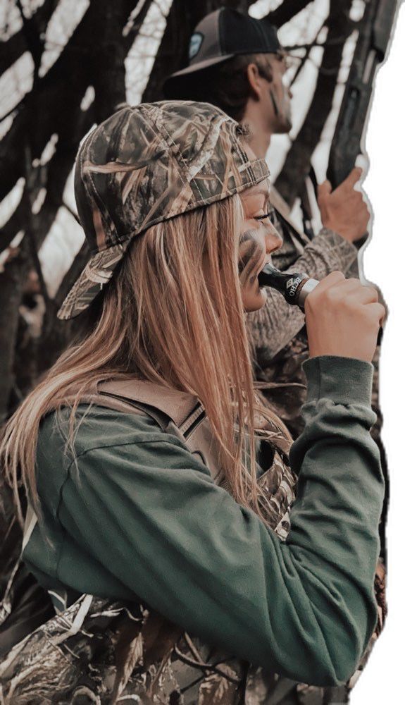 a man and woman standing next to each other in front of trees with hunting gear