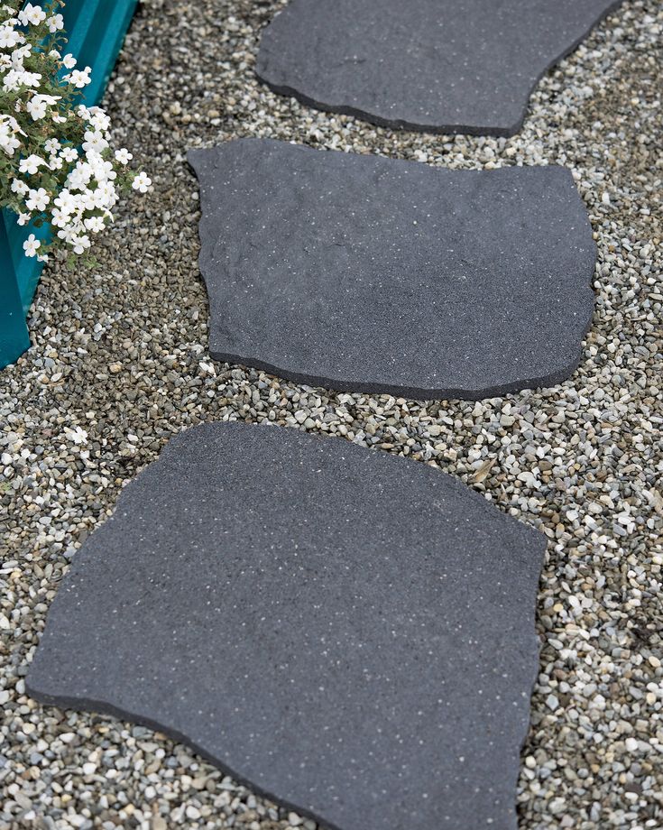 two black stones sitting on top of gravel next to a planter filled with white flowers