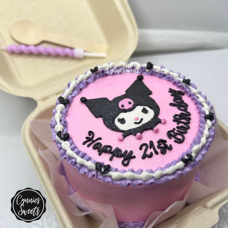 a pink and black birthday cake sitting in a box next to a container with spoons