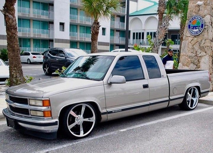 a silver truck is parked on the side of the road in front of some palm trees