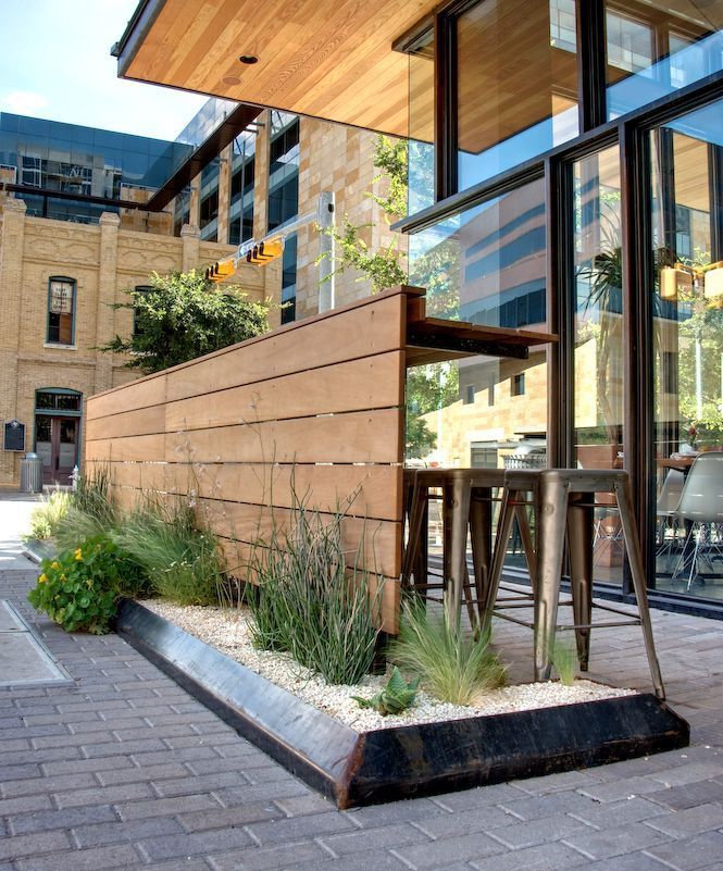 an outdoor dining area in front of a building with large windows and plants on the side