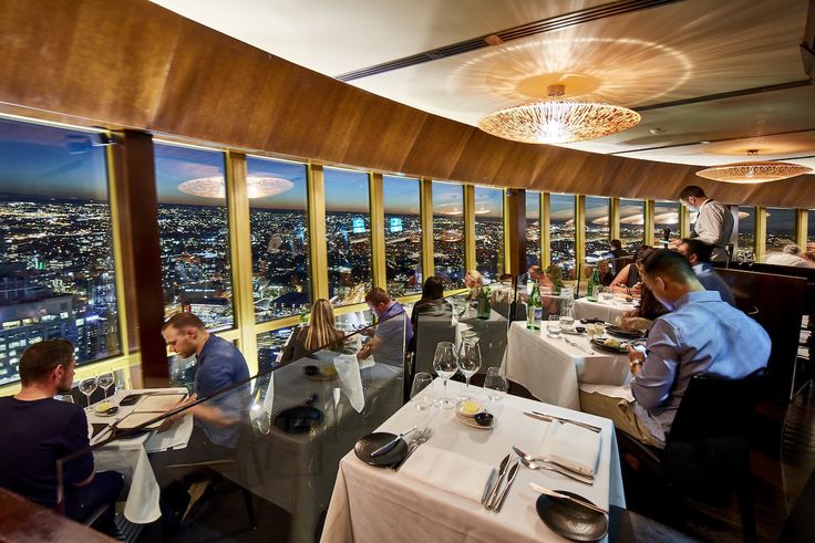 people sitting at tables in a restaurant overlooking the city