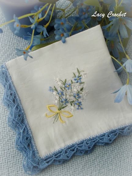 a white handkerchief with blue flowers on it next to a candle and some blue flowers