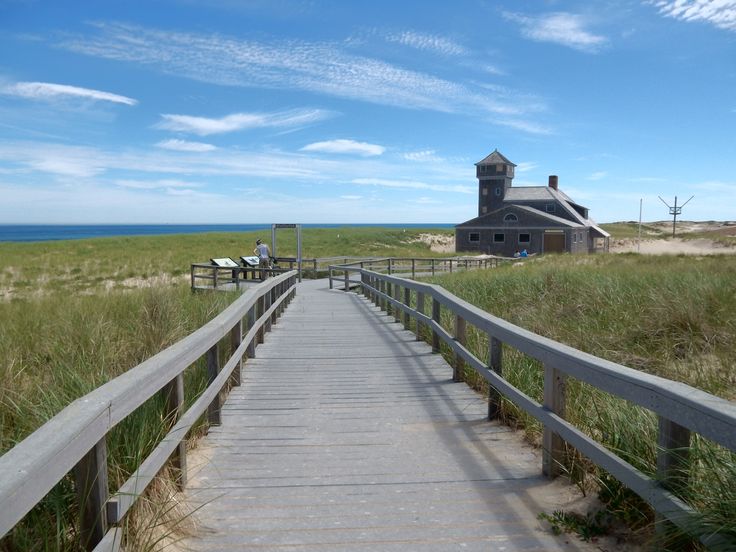 a wooden walkway leading to an old building on the beach with grass and sand around it