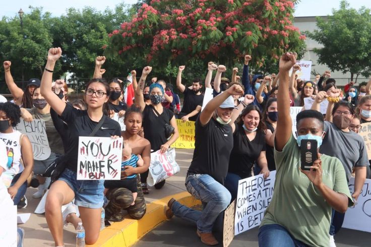 a group of people holding up signs and cell phones in front of a building with trees