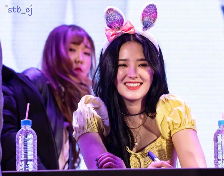 two young women sitting at a table with water bottles and bunny ears on their head