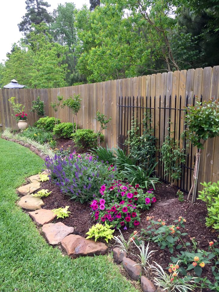 a garden with lots of flowers and plants in the grass next to a wooden fence