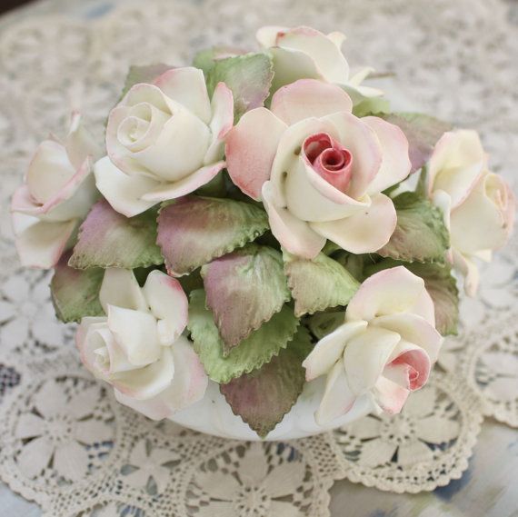 a bouquet of flowers sitting on top of a lace tablecloth covered doily with white and pink roses