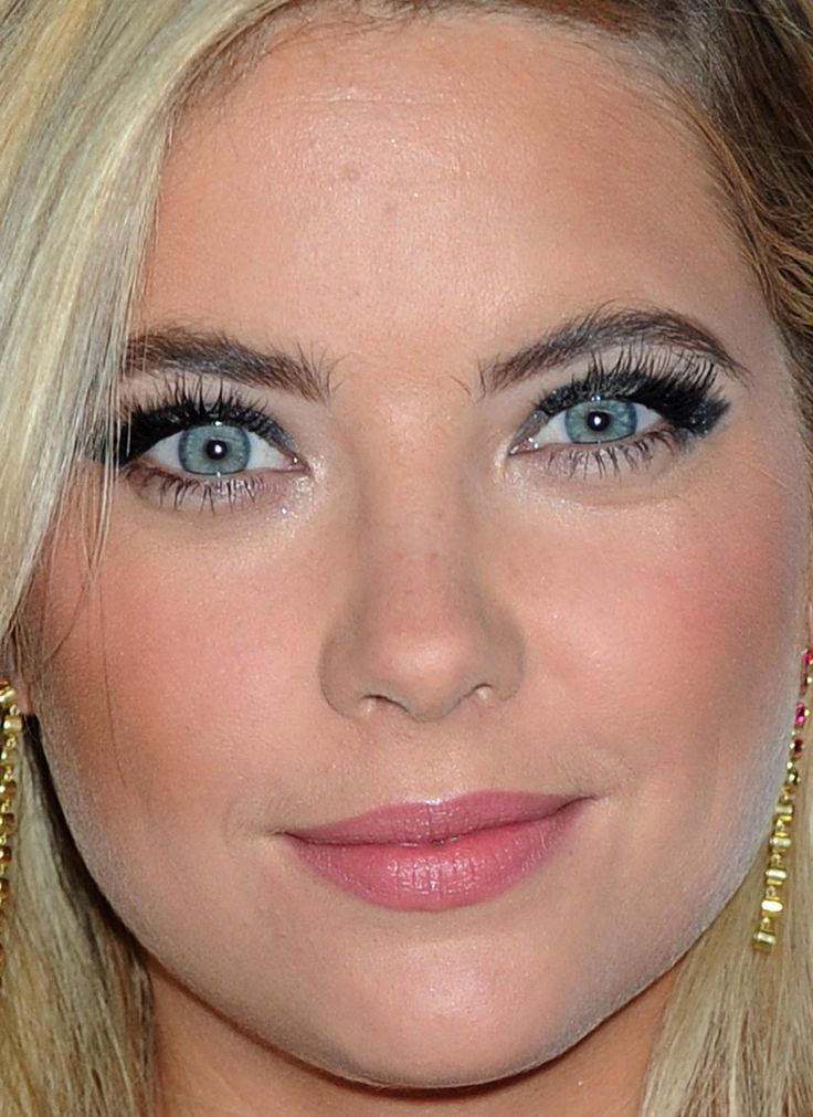 a close up of a woman with blue eyes and blonde hair wearing gold ear rings