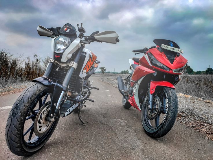 two motorcycles parked side by side on the road with cloudy skies in the back ground