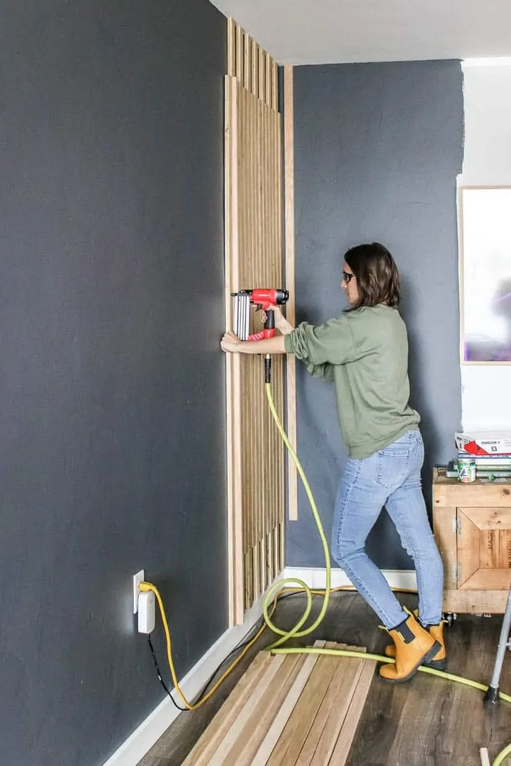 a woman is using a power drill to install a wall panel in her living room