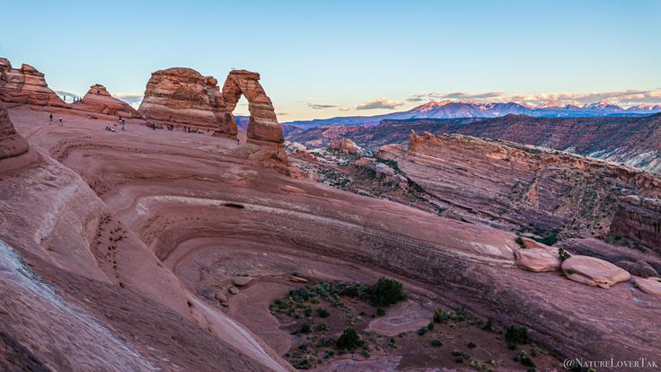 people are standing on the edge of a cliff in the desert at sunset or dawn