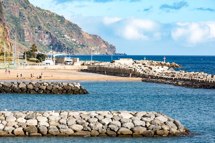 people are swimming in the ocean near some rocks and water with mountains in the background