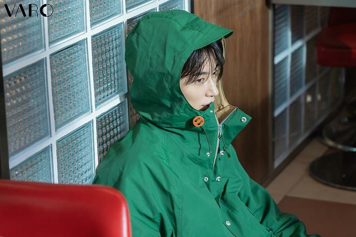 a person wearing a green rain coat sitting on a red chair in front of a wall