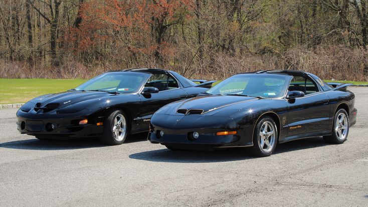 two black sports cars parked next to each other in a parking lot with trees in the background