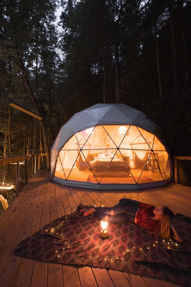 a person laying on a blanket in front of a glass dome tent with lights inside