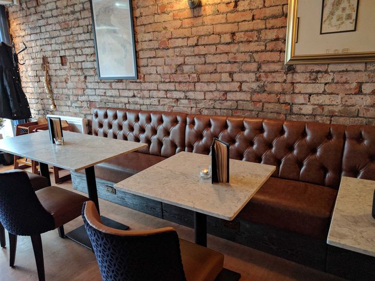 an empty restaurant with brown leather booths and white tables in front of a brick wall