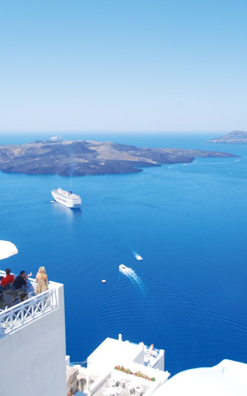 people are sitting on the roof of a building overlooking the ocean and boats in the water