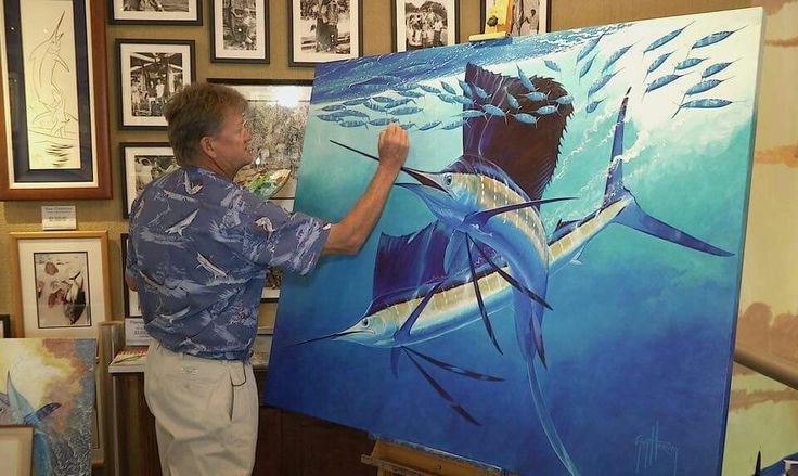 a man is painting on an easel in front of some framed pictures and paintings