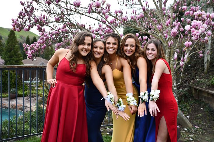 a group of women standing next to each other in front of a tree with purple flowers